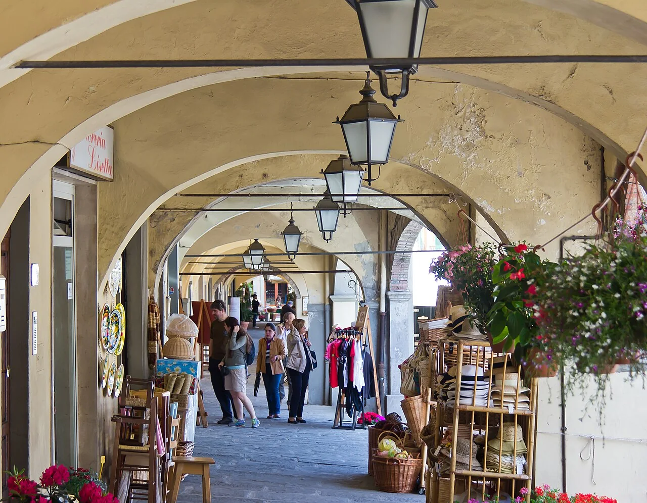 Visitors under Greve’s ochre covered arcades, with baskets, shops and café chairs